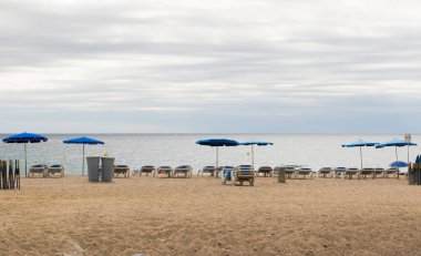 Kumlu deniz kumsalı, güneşli yataklar, yaklaşan yağmur fırtınalı şemsiye. Kötü hava ile tatil.