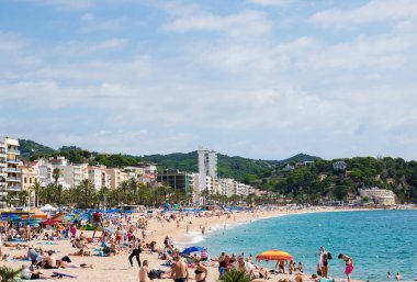 Sahilde evler, kum, palmiye ağaçları, deniz, bikinili insanlar, dağ, yaz günü oteller. İspanya.