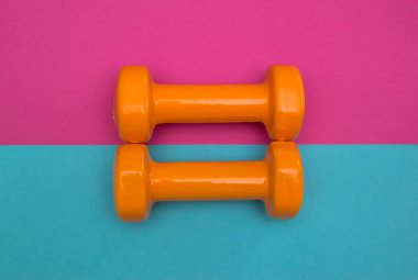 Pembe ve mavi arka planda iki turuncu dambıl. Yaz zamanı eğitim, spor ve etkinlik için bir araçtır.