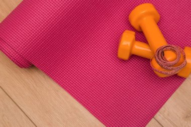 Spor salonunda pembe yoga minderinde iki turuncu dambıl ve rulet. Yaz zamanı eğitim, spor ve etkinlik araçları.