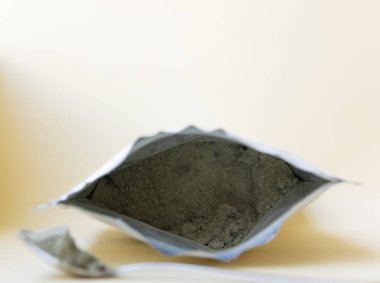 Pakette yeşil bitkisel toz var. Arka planda metal kaşık var..