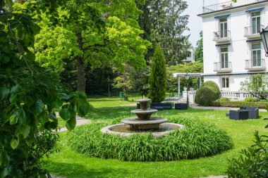 Baden-Baden 'de bir otelin yanındaki çeşme ve yaz bahçesi. Bağbozumu lambaları, ağaçları, çiçekleri ve yeşil otları olan doğa arka planı. 