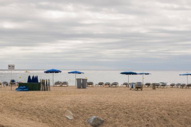 Kumlu deniz kumsalı, güneşli yataklar, yaklaşan yağmur fırtınalı şemsiye. Kötü hava ile tatil.