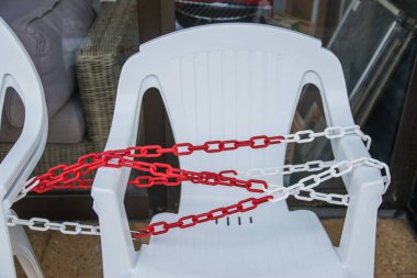 Dükkânın yanındaki yazlık kafede zincirli beyaz plastik sandalyeler..