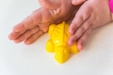 Küçük çocuğun iki eli tahta arka planda küçük oyuncağı tutuyor. Sarı plastik kaplumbağa..