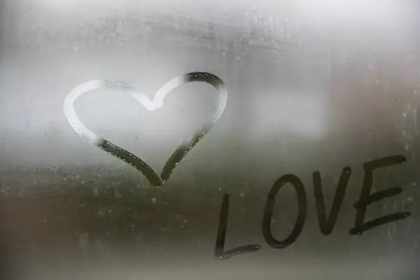 Beautiful heart symbol and love word on the glass window with water drobs.