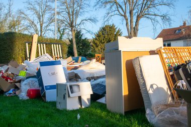 Ev yakınlarındaki bir şehirde çok fazla atık var. Eski ahşap mobilyaları, oyuncakları, kutuları, sokakta plastik torbaları ve Almanya 'da bahar güneşli çöplük gününde yeşil çimenleri olan büyük bir çöp.. 