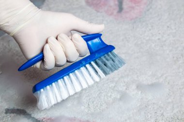 Temizlik için fırçayı tutan lastik eldiveni ver. Yerleri temizlemek için plastik mavi fırça ve köpük.. 