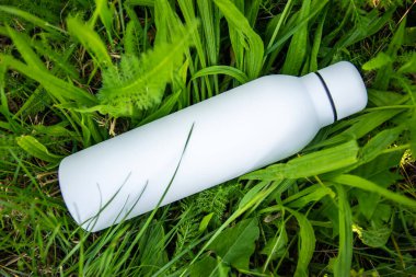 Suyu yeşil çimen arka planında beyaz termo paslanmaz şişede tazeliyorum..