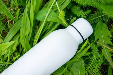 Suyu yeşil çimen arka planında beyaz termo paslanmaz şişede tazeliyorum..