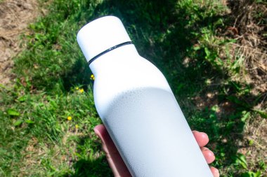 Beyaz termodinamik paslanmaz şişe. Elinde ferahlatıcı su var..