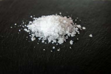 Siyah arka planda beyaz tuz kristalleri var. Lokantanın yemeklerini pişirmek için tuz kristalleri..
