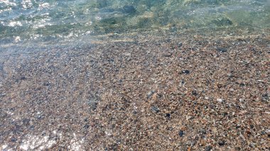 Deniz taşları. Güneşli bir günde şeffaf su ve dalgalar çok taşlı..