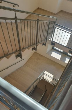 Binanın içinde mermer taştan bej merdivenler ve metal parmaklıklar olan iç merdiven. Sarmalın yakın görüntüsü.