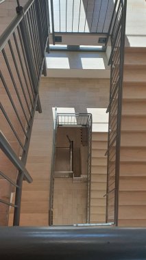 Binanın içinde mermer taştan bej merdivenler ve metal parmaklıklar olan iç merdiven. Sarmalın yakın görüntüsü.