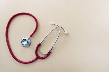 Red stethoscope on beige background with space for text. Medical instrument. Health care concept.