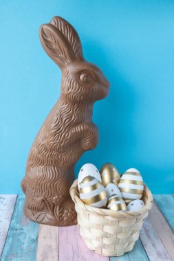 Mavi arka planda Paskalya tavşanı şeklinde çikolata ve yumurtalı sepet..