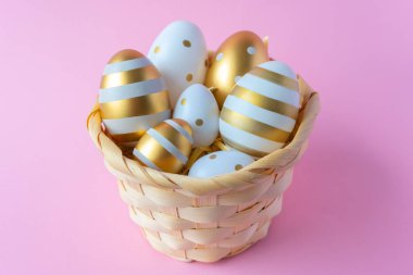 Pembe arka planda dokuma doğal sepetinde altın Paskalya yumurtaları. Tebrik kartı için Paskalya konsepti.