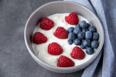 Doğal taze Yunan yoğurdu, ahududu, böğürtlen ve siyah tabakta ve peçeteyle sağlıklı kahvaltı.. 