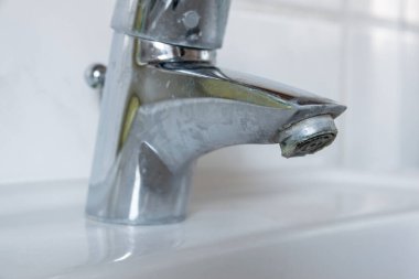 Water dripping of lime on metal tap. Durty faucet in bathroom.
