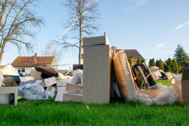 Ev yakınlarındaki bir şehirde çok fazla atık var. Eski ahşap mobilyaları, oyuncakları, kutuları, sokakta plastik torbaları ve bahar güneşli çöp atma gününde yeşil çimenleri olan büyük bir çöp.. 