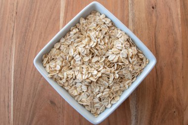 Sağlıklı kahvaltı için beyaz porselen tabakta kuru yulaf gevreği ya da ahşap masada süt..