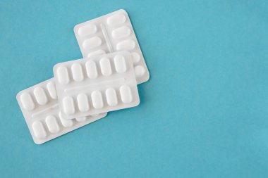 Mavi arka planda beyaz plastik pakette bir sürü ilaç ve ilaç var. Sağlık hizmetleri kavramı.