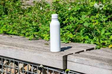 Tazeleyici suyu olan beyaz termodinamik paslanmaz şişe parktaki bankta çok sayıda yeşil kadife ile kal..