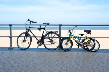 Yetişkinler ve çocuklar deniz sahilinin yakınındaki caddede klasik bisikletler. Mavi deniz, sarı kum ve yaz gökyüzü. Spor ya da seyahat için bisiklet