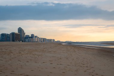 İnsanlar akşamları deniz kenarındaki kumsalda bir sürü ev ve otelle yürüyorlar. Ostend, Belçika 'da kum, rahatlama ve gün batımı.