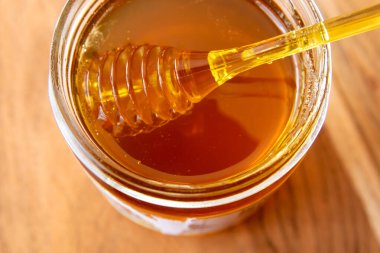 Ballı cam kavanoz bal peteği ve sarı kaşık ahşap masada kalsın..