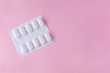 Pembe arka planda beyaz plastik pakette bir sürü ilaç ve ilaç var. Sağlık hizmetleri kavramı.