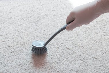 Beyaz kauçuk eldiven, yerde köpük beyazı halı ve temizlik için gri fırçayı tut.. 