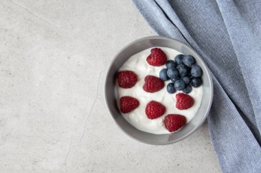 Gri tabakta kırmızı ve siyah böğürtlenli doğal taze Yunan yoğurdu ve sağlıklı kahvaltı için peçete.. 