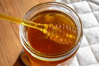 Ballı cam kavanoz bal peteği ve sarı kaşık ahşap masada ve peçetede kalsın..