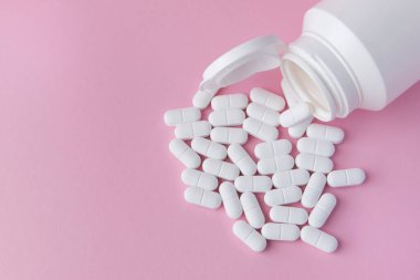 Beyaz haplar ve pembe arka planda plastik şişede uyuşturucular. Sağlık sigortası konsepti. Metin için boşluk.