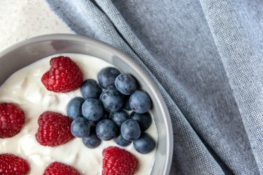 Gri tabakta kırmızı ve mavi böğürtlenli doğal taze Yunan yoğurdu ve sağlıklı kahvaltı için peçete. Siyah taş arkaplan.