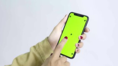 Gömlekli bir kadın beyaz arka planda yeşil ekran akıllı telefon kullanıyor.