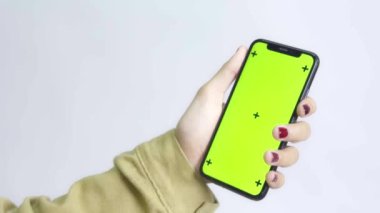 Gömlekli bir kadın beyaz arka planda yeşil ekran akıllı telefon kullanıyor.