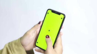 Gömlekli bir kadın beyaz arka planda yeşil ekran akıllı telefon kullanıyor.