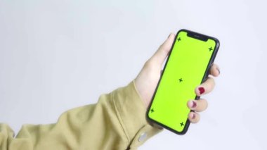 Gömlekli bir kadın beyaz arka planda yeşil ekran akıllı telefon kullanıyor.