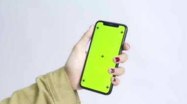 Gömlekli bir kadın beyaz arka planda yeşil ekran akıllı telefon kullanıyor.