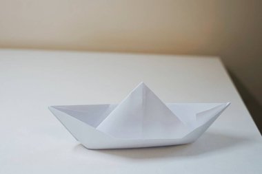 Origami, bej duvar çalışması masasındaki boş bir hücredeki beyaz boş bir kağıttan yapılmış kağıttan bir tekne hobi yapar. Yüksek kalite fotoğraf