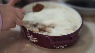 Küçük kız ev yapımı tiramisu keki yapmaya yardım ediyor tatlı üzerine kakao tozu dökülüyor ve dökülmüş odun dökülüyor. Yüksek kalite 4k görüntü