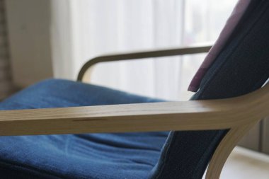 Ahşap çerçeveli mavi yastıklı koltuğun yakın görüntüsü, yumuşak ışıklandırılmış arka planda doku tasarımını vurguluyor. İdeal mobilya, iç tasarım konseptleri Yüksek kaliteli fotoğraf