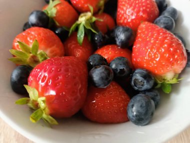 Beyaz bir kasede çilek ve yaban mersini yaz mevsimi taze kırmızı mavi sağlıklı meyveler. Yüksek kalite fotoğraf