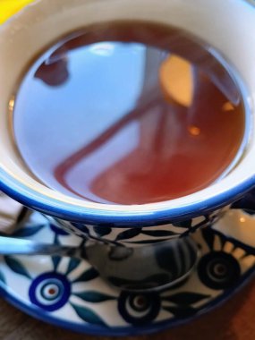 Buharı tüten bir çay bardağının yakından görüntüsü. Karmaşık desenli bir çay tabağının üzerinde dinleniyor. Samimi anlar için mükemmel..