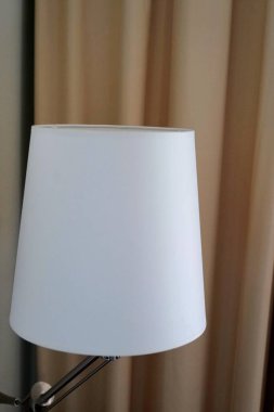 Yumuşak bej perdelere kurulmuş minimalist beyaz bir abajur, sakin ve sakin bir atmosfer yaratıyor. Modern iç tasarım için mükemmel..