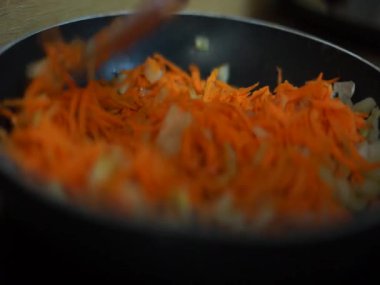 Siyah bir tavada kızartılan taze havuç ve soğanların görüntüsü, canlı renkler ve pişirme teknikleri sergiliyor..