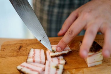 Keskin bir bıçakla domuz pastırmasını ustalıkla dilimlemek, yemek hazırlama tekniklerini ön plana çıkarmak..